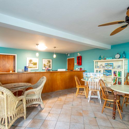 A cozy waiting area with wicker and wooden chairs, a reception desk, brochures on a rack, and a ceiling fan. Bright and inviting atmosphere.