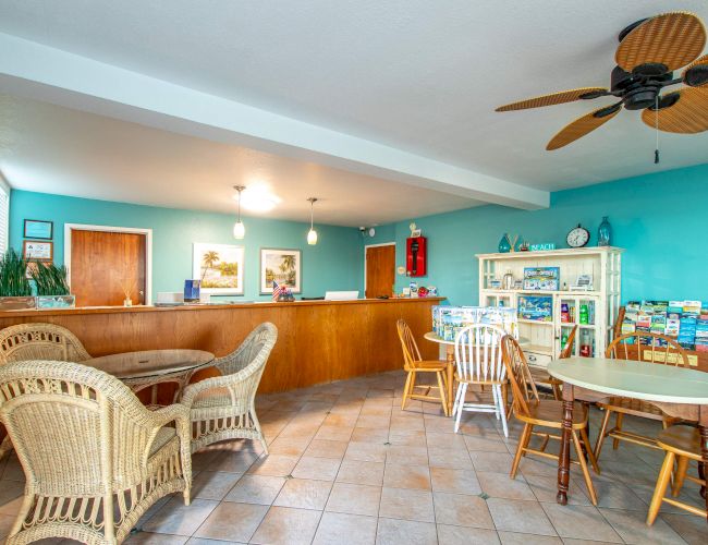 A cozy waiting area with wicker and wooden chairs, a reception desk, brochures on a rack, and a ceiling fan. Bright and inviting atmosphere.