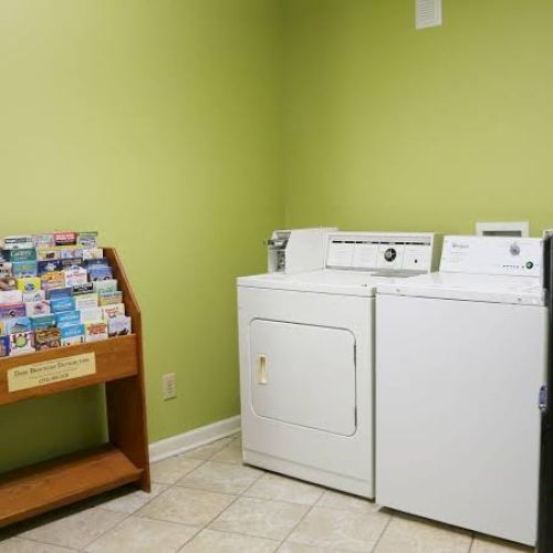 The image shows a laundry room with a washing machine, dryer, brochure stand, and green walls.