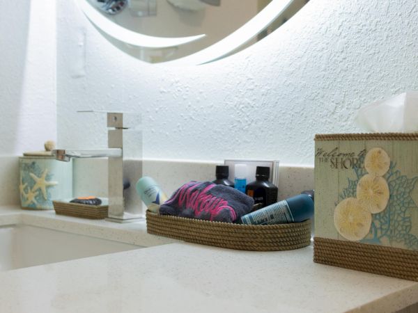 A bathroom countertop with a faucet, tissue box, and a basket of toiletries near a round mirror.