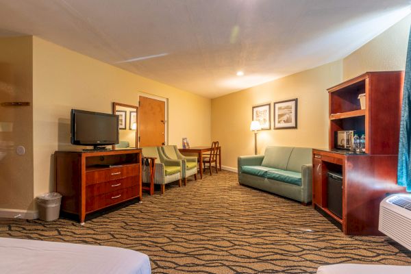 A hotel room with a TV, sofa, and chairs, featuring a wooden cabinet and table with framed pictures on the wall.