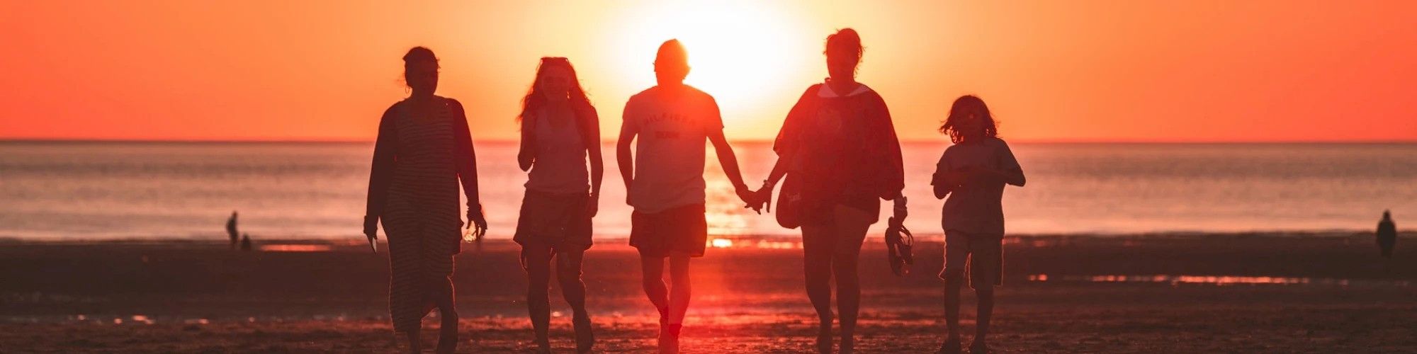 Silhouettes of five people walking hand in hand on a beach during a vibrant sunset over the ocean, creating a warm and serene atmosphere.