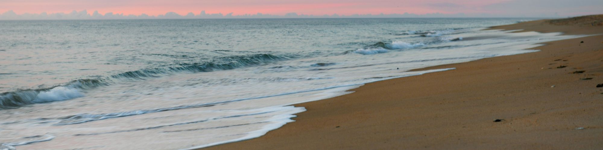 A serene beach scene with gentle waves lapping at the sandy shore under a pastel-colored sky at sunset.