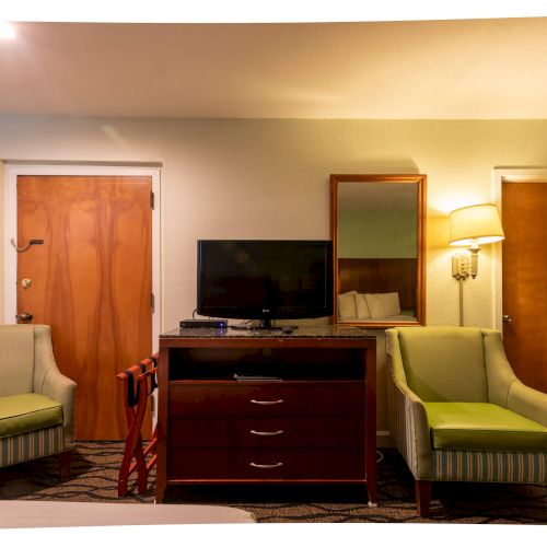 The image shows a hotel room with two chairs, a TV on a dresser, a wall mirror, and a lamp. There are two wooden doors visible.