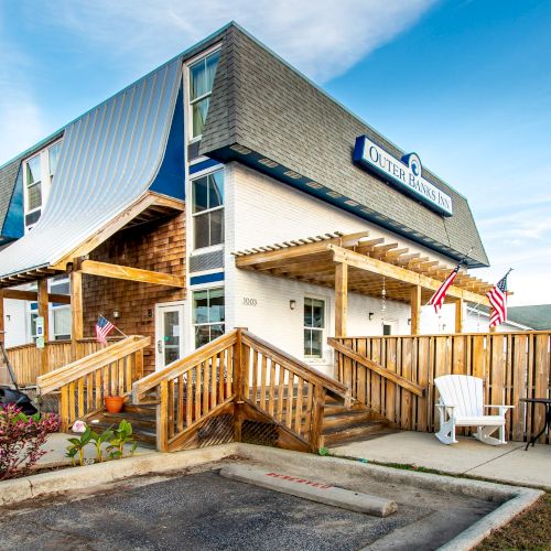 The image shows a building with a sloped roof, a wooden deck, and American flags, likely an Inn or lodge, with outdoor seating.