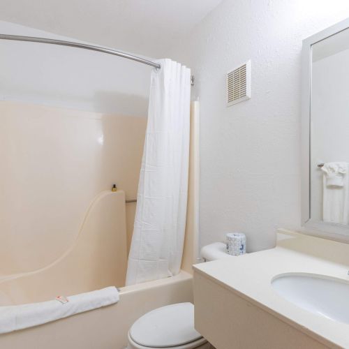 A bathroom with a bathtub, shower curtain, towels, sink, mirror, and toilet in a compact, well-lit space.