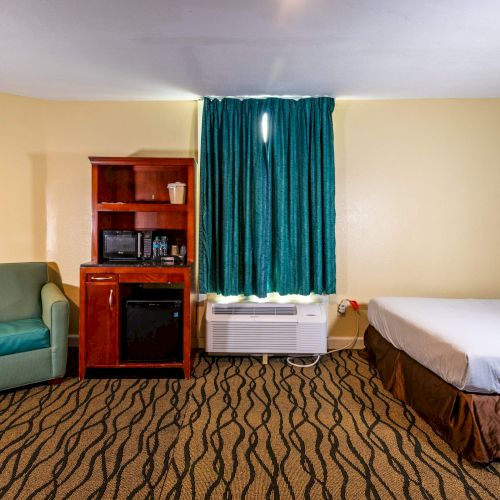 The image shows a hotel room with a bed, a green couch, a wood cabinet with a microwave, and teal curtains. Carpet has a wavy pattern.