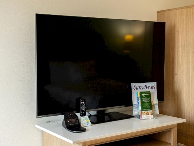 A flat-screen TV on a wooden cabinet with a phone, remote, and a magazine beside it.