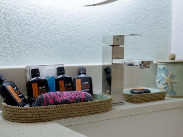 A bathroom countertop with toiletries in a woven basket, a modern faucet, and a decorative container with a starfish design.