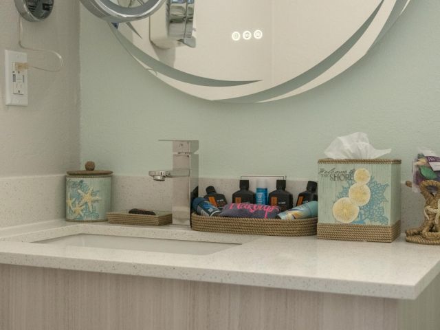 A bathroom countertop with a sink, mirror, tissue box, and a tray with toiletries, set against a soft-colored wall, creates a tidy space.